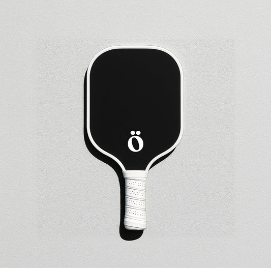 Minimalist black and white Evöq pickleball paddle with matte finish and ö logo, displayed on green court background. Lightweight performance gear for modern players.
