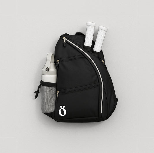 Sleek black Evöq pickleball backpack with white zippers, holding two paddles and a water bottle. Stylish gear bag for on-the-go athletes.